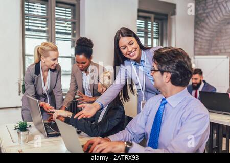 Lächelnder junger Manager, der leitenden Angestellten bei der Arbeit mit Computern im Büro hilft, Mentorenausbildung, glücklicher älterer Mitarbeiter am Arbeitsplatz. Stockfoto
