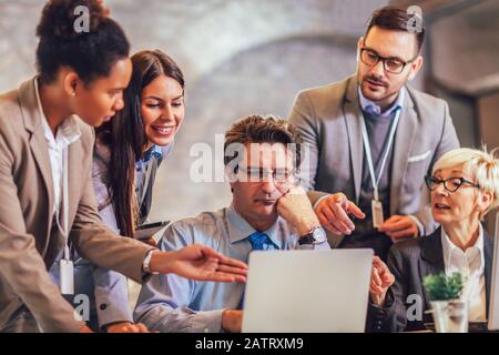 Lächelnder junger Manager, der leitenden Angestellten bei der Arbeit mit Computern im Büro hilft, Mentorenausbildung, glücklicher älterer Mitarbeiter am Arbeitsplatz. Stockfoto