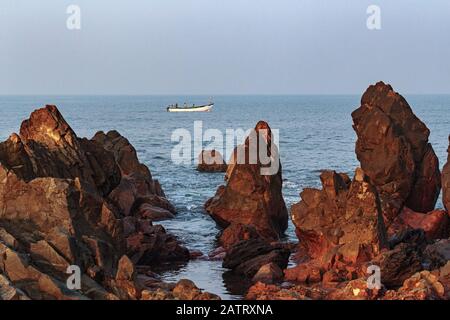 Morgendliches Seascape. Schöne Klippen in Ufernähe und ein Fischerboot. Fischer fangen am frühen Morgen Fisch. Arambol, Goa, Indien Stockfoto