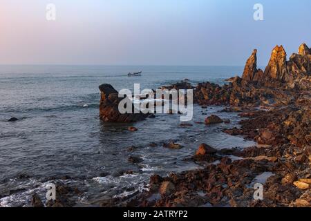 Morgendliches Seascape. Schöne Klippen in Ufernähe und ein Fischerboot. Fischer fangen am frühen Morgen Fisch. Arambol, Goa, Indien Stockfoto