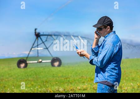 Landwirt mit einem Tablet und Smartphone auf einem Feld mit Bewässerung; Alberta, Kanada Stockfoto