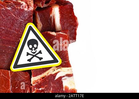 Konzept für schädliche Bakterien in Fleisch für den menschlichen Verzehr, die Brocken von rotem Fleisch mit gelbem Schädel giftiges Warnschild und leerem weißen Kopierraum zeigen Stockfoto