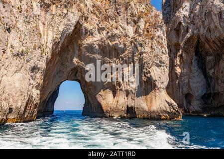 Natürlicher Bogen in den Kalksteinfelsen der Faraglioni Felsen mit Blick auf ein Boot, Insel Capri am Tyrrhenischen Meer, Mittelmeer Stockfoto