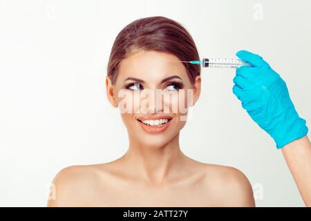 Frau, die im medizinischen Büro Hyaluronsäure Botulinumtoxin auf die Stirn spritzt und glücklich lächelnd zur Seitennadel schaut Stockfoto