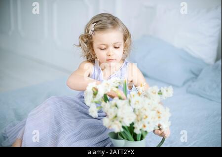 Mädchen hält Narzisse in Händen. Liebenswürdig lächelndes kleines Mädchen, das am Muttertag Blumen für ihre Mutter hält Stockfoto