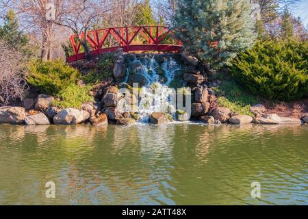 Eine Wasserattraktion einer kleinen Truss-Fußgängerbrücke und eines Wasserfalls an einem kleinen See im Einkaufszentrum Bradley Fair in Wichita, Kansas, USA. Stockfoto