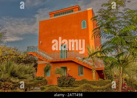 Ein viereckiges rotes ockergezungtes Haus unter den Palmen im Sonnenschein gegen einen blauen Himmel, El Gouna, Ägypten, 12. Januar 2020 Stockfoto