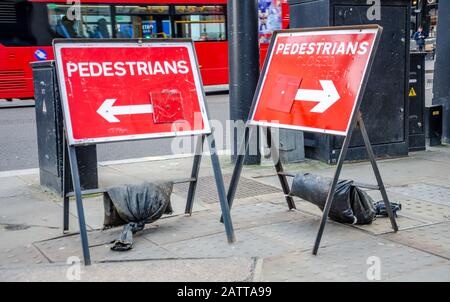 Hinweisschilder zeigen in entgegengesetzte Richtungen, um Fußgänger anzuweisen, wohin sie gehen sollen, um eine blockierte Strecke wegen Bauarbeiten zu vermeiden. Stockfoto