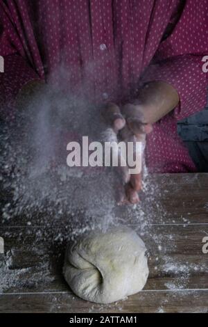 Eine Frau klatscht sich die Hände um den Go herum und spritzt Mehl. Prozess der Zubereitung von Teig zum Backen von Brot Stockfoto