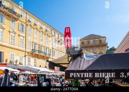 Touristen und Franzosen genießen einen geschäftigen Einkaufsbummel auf dem Flohmarkt Cours Saleya neben den gelben Apartments und Bars und Cafés in Der Altstadt. Stockfoto