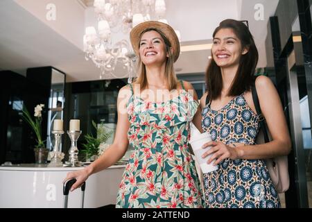 Porträt zweier junger Freunde, die im Hotel ankommen und mit ihrem Gepäck durch die Lobby laufen. Reise- und Lifestyle-Konzept. Stockfoto