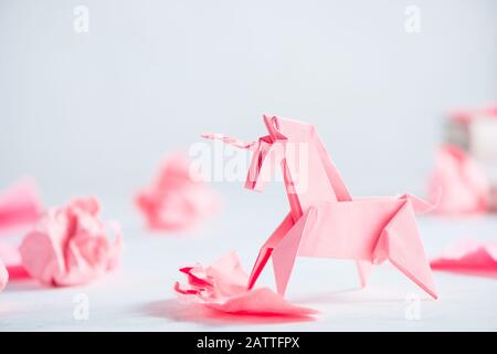 Pinkes Origami-Einhorn mit zerknitterten Papierkugeln. Der kreative Prozess ist das Schreiben, der helle Hintergrund Stockfoto