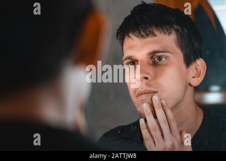 Junger gutaussehender Mann, der seinen Bart vor dem Spiegel betrachtet. Pflegekonzept. Stockfoto