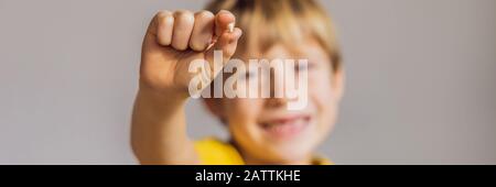 Der kaukasische Junge der Litle hält einen abgesenkten Milchzahn zwischen seinen Fingern und lacht mit Blick auf das lange FORMAT des KAMERA-BANNERS Stockfoto