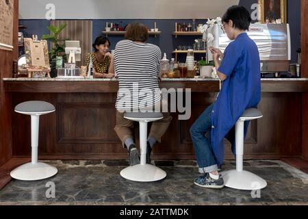 Menschen, die auf Hockern in einer Bar im Café-Innenbereich sitzen und eine Frau, die sich in das Stricken verstrickt hat Stockfoto