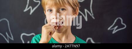 Der kaukasische Junge der Litle hält einen abgesenkten Milchzahn zwischen seinen Fingern und lacht mit Blick auf das lange FORMAT des KAMERA-BANNERS Stockfoto