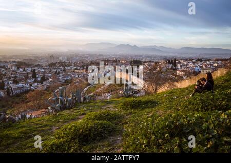 Granada, Spanien - 17. Januar 2020: EIN Paar blickt auf Granada bei Sonnenuntergang an den Albaicin-Stadtmauern am San Miguel Alto Aussichtspunkt. Stockfoto