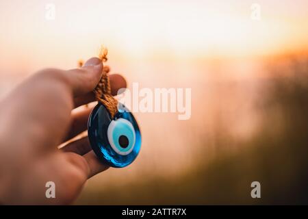 Der Mensch hält bei Sonnenuntergang böse Augenwulst in der Hand. Kulturkonzept. Stockfoto