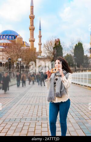 Wunderschöner Tourist isst traditionelle Straßennahrung Simit oder Bagel auf Englisch mit Blick auf die Sultanahmet-Moschee oder die Blaue Moschee, ein beliebtes Ausflugsziel in Stockfoto