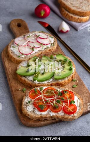 Sandwiches mit Mikrogrüns und Gemüse auf einer Schneideplatte auf einem Betonhintergrund. Nahaufnahme Stockfoto