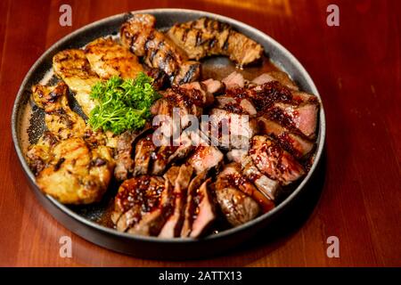 Frische, saftige Sortiment von geschnittenen Fleisch vom Grill, die auf eine große und runde Platte liegt, mit Petersilie auf der Oberseite dekoriert. Stockfoto