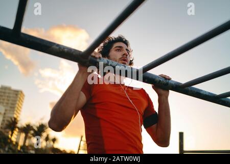 Nahaufnahme eines jungen männlichen Athleten, der Übungen an der Bar im Fitnesspark gegen Himmel macht - Mann, der im Freien Pull-ups macht Stockfoto