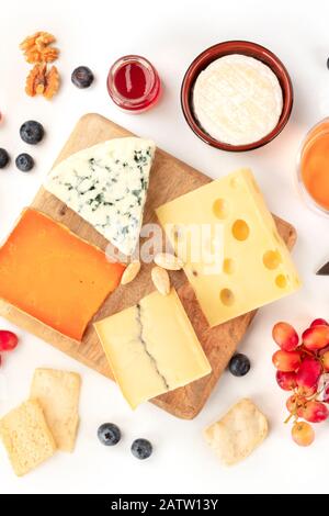 Käseplatte, ein flaches Lay-Shirt auf weißem Hintergrund. Blaukäse, holländischer Käse und andere, eine Vielfalt mit Früchten und Nüssen Stockfoto