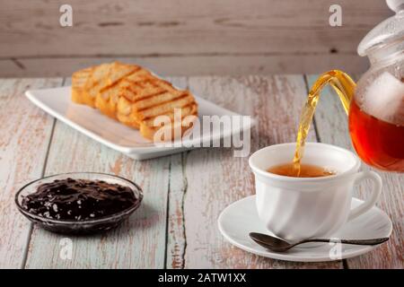 Frisch zubereiteter Tee in einer Teekanne mit Plätzchen und Marmelade auf dem Tisch Stockfoto