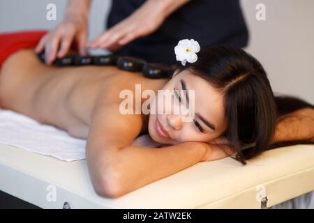 Junge Asianerin, die die therapeutischen Auswirkungen einer traditionellen Hot-Stone-Massage im luxuriösen Spa- und Wellness-Center genießt. Stockfoto