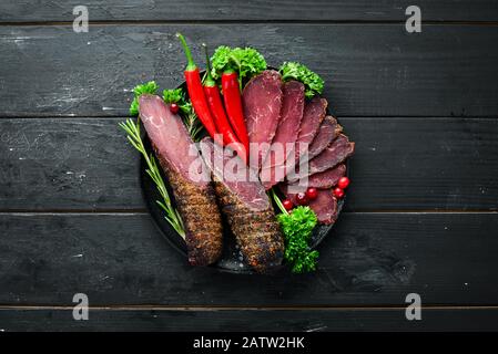 Getrocknetes Kalbsfleisch mit Gewürzen und Kräutern. Rindfleisch auf altem schwarzen Tisch ruckartig. Draufsicht. Freier Speicherplatz für Ihren Text. Stockfoto