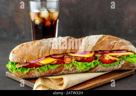 Ein Sandwich mit dunklem Brot mit Salat, Speck, Tomaten, Käse und Zwiebeln. Baguette. Frühstück. Fast Food. Gesunde Ernährung. Rezepte. Stockfoto