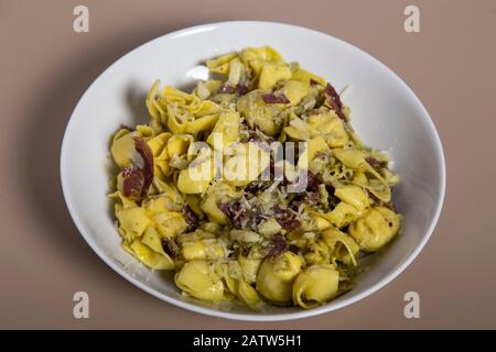 Gebackene Käse-Tortellini- oder Bauchnopfnudeln mit iberischem Schinken auf Holzhintergrund. Stockfoto