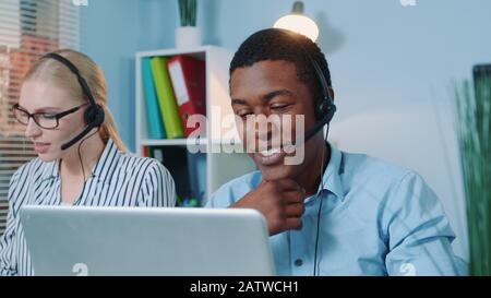 Nahaufnahme eines freundlichen afrikaners, der in Callcentern arbeitet. Er nimmt den internationalen Anruf in einem Headset entgegen. Stockfoto