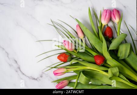 Nahaufnahme eines schönen Blumenstraußes mit roten Erdbeeren auf einem Marmortisch mit Platz für Text. Frühling, Sommer, Tulpen Stockfoto