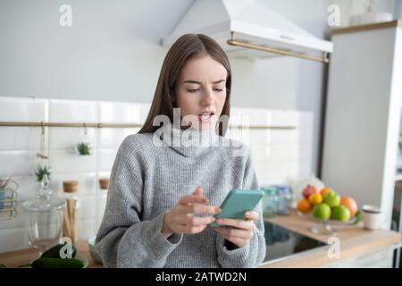 Dunkelhaariges Mädchen in einem grauen Pullover, der interessiert aussieht Stockfoto