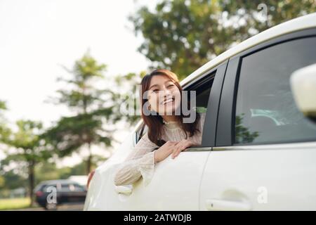 Porträt der glückliche junge Frau, die auf einem Road Trip lehnte sich aus dem Fenster. Weibliche genießen Reisen in einem Auto mit ihrem Freund. Stockfoto