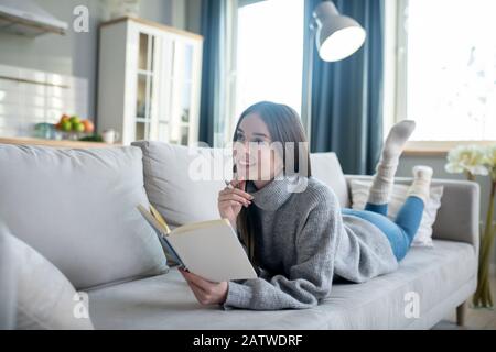 Junges Mädchen in einem grauen Pullover, das über eine neue Idee nachdenkt