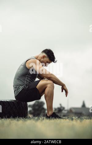 Seitenansicht des jungen Athleten, der sich nach einem intensiven Flip-Workout im Freien müde fühlt. Muskulöser Mann, der eine Pause vom Kreuztraining auf einem Feld nimmt. Stockfoto