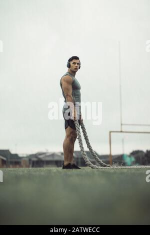 Mann, der sich vom Kampfseiltraining ausruhen kann. Muskelmann, der Fitness-Workout macht, während es mit Schlagseilen auf einem Feld regnet. Stockfoto