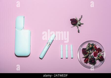 Weiße elektronische Zigarette und verwelkte Rosen auf pinkfarbenem Hintergrund. IQoS mit roten getrockneten Blumen, Draufsicht Stockfoto