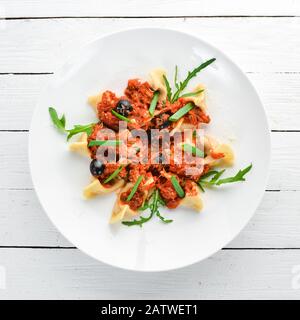 Ravioli mit Fleisch- und Tomatensauce und Oliven. In einer Platte auf Holzhintergrund. Draufsicht. Freier Speicherplatz. Stockfoto