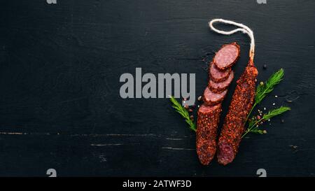 Wurst Paperoni. Salami mit Paprika. Auf schwarzem Holzhintergrund. Draufsicht. Freier Speicherplatz für Ihren Text. Stockfoto