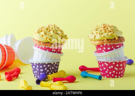 Lustige Cupcakes in lustigen Polka-Punktbechern und abgeplatzte Ballons auf gelbem Hintergrund, Nahaufnahme, Kopierraum Stockfoto