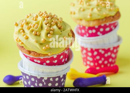 Lustige Cupcakes in lustigen Polka-Punktbechern und abgeplatzte Ballons auf gelbem Hintergrund, Nahaufnahme, Kopierraum Stockfoto