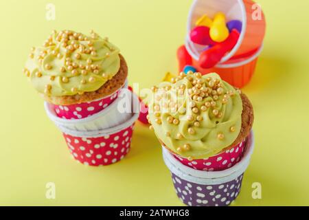 Lustige Cupcakes in lustigen Polka-Punktbechern und abgeplatzte Ballons auf gelbem Hintergrund, Nahaufnahme, Kopierraum Stockfoto