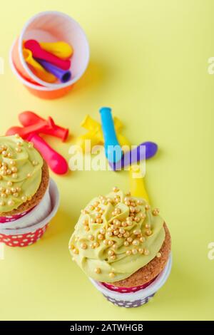 Lustige Cupcakes in lustigen Polka-Punktbechern und abgeplatzte Ballons auf gelbem Hintergrund, Nahaufnahme, Kopierraum Stockfoto