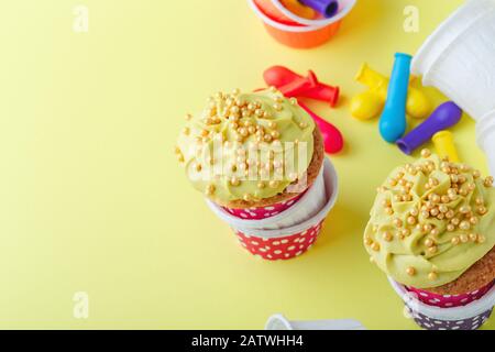 Lustige Cupcakes in lustigen Polka-Punktbechern und abgeplatzte Ballons auf gelbem Hintergrund, Nahaufnahme, Kopierraum Stockfoto