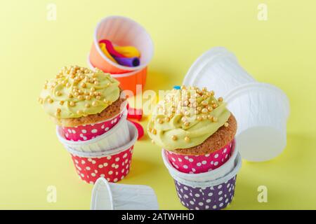 Lustige Cupcakes in lustigen Polka-Punktbechern und abgeplatzte Ballons auf gelbem Hintergrund, Nahaufnahme, Kopierraum Stockfoto