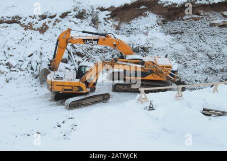 Zwei gelbe Raupenbagger graben im Winter in der Grube Boden. Schwere Maschinen arbeiten an einer Baustelle. Stockfoto