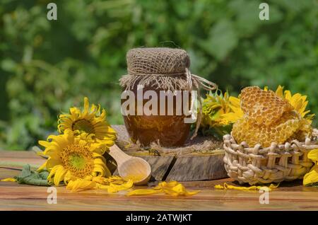 Honig mit Honigabipper auf Holztisch. Organischer Blumenhonig vor verschwommenem Hintergrund mit Blumen Stockfoto